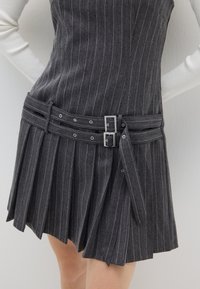 Vestido gris oscuro con rayas verticales blancas, que presenta un corsé ajustado, falda plisada y un doble cinturón con hebillas en tono plateado.