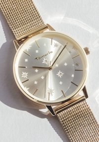 Montre avec un bracelet en maille dorée et un cadran argenté à motif d'étoiles, avec des index horaires dorés et le nom de la marque "Tamaris" au centre.