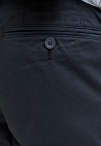 Μαύρο παντελόνι από ύφασμα με απαλή υφή, που διαθέτει ορατή λεπτομέρεια με κουμπί και ραφή κοντά στην τσέπη για επιπλέον σχεδιασμό.