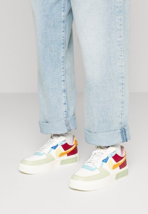 Lyseblå jeans med opkrogede bukseben, båret sammen med hvide sneakers med flerfarvede paneler i rød, orange, blå og lysegrøn.