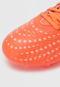 Zapatilla de fútbol de color naranja brillante con parte superior texturizada que presenta patrones de puntos blancos, cordones y una puntera redondeada. Diseñada para tracción y agilidad.