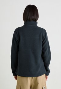 Ciemnoszara kurtka polarowa z wysokim kołnierzem i fakturowaną tkaniną. Posiada szew wzdłuż środkowej części oraz długie rękawy.