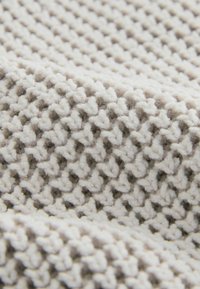 Textil tricotat de culoare gri deschis, cu o suprafață texturată și patternată, având forme mici, ridicate și interconectate. Material moale și gros.