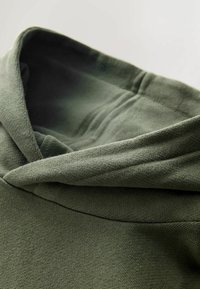 Felpa verde oliva con un tessuto morbido e testurizzato. Il cappuccio è foderato e c'è una cucitura visibile lungo la scollatura.