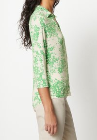 Grön pikétröja med blommönster och trekvartsärmar, tillverkad av ett lätt tyg, med krage och rak nederkant.