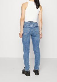 Ljusblå denimjeans med slim fit, synlig sömnad och dubbel bakficka, tillsammans med en vit ribbad linne och svarta skor.