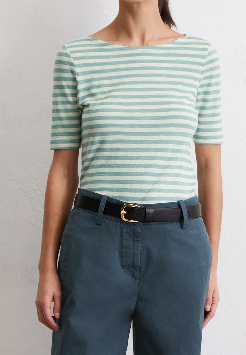 Mujer vistiendo una blusa de rayas verde menta y blanca de mangas cortas metida dentro de pantalones verde azulado oscuros con un cinturón negro con una hebilla dorada.
