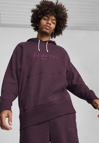 Lilla hættetrøje med kengurulomme, snorhætte og broderet "Sportswear by PUMA." Blødt, tekstureret stof.