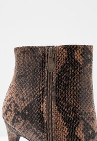 Stivaletto in pelle di serpente marrone e nero con superficie texturizzata e zip laterale per la chiusura. Il tacco a spillo aggiunge altezza.