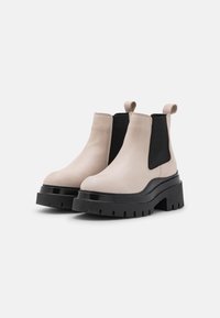 Botas Chelsea de piel beige con paneles elásticos laterales negros, plataforma gruesa negra y tira de agarre. Textura lisa y diseño de punta redondeada.