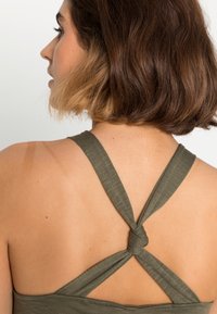 Camisola de alças verde-oliva com alças cruzadas nas costas e detalhe de nó, feita de um tecido suave e texturizado.