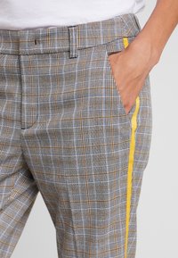 Szare spodnie w kratę z żółtym paskiem bocznym, wykonane z teksturowanej tkaniny, z płaskim przodem i bocznymi kieszeniami. Minimalistyczny design z dopasowanym krojem.