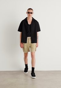 Maglietta nera a maniche corte con texture, canotta nera, pantaloni cargo beige con tasche laterali, calzini neri alla caviglia e sneakers nere.