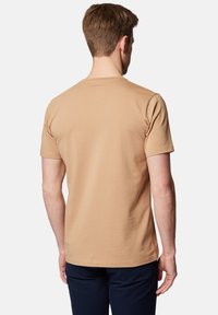 Beżowy t-shirt z krótkim rękawem wykonany z miękkiej bawełny, z prostym okrągłym dekoltem i metką z logo na górnej części pleców. Gładka tekstura.