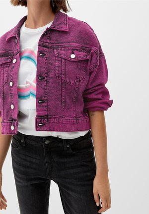 Osoba w żywiołowej fioletowej kurtce dżinsowej noszonej na białej koszulce z nadrukiem oraz czarnych dżinsach, z rękawami swobodnie podwiniętymi.