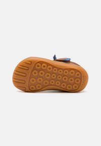Chaussures marron avec une semelle en caoutchouc texturée présentant des motifs circulaires et une sangle d'accent bleu. Design robuste idéal pour un usage décontracté.