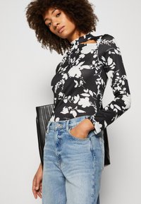 Svarte og hvite blomstermønstrede bodysuit med lange ermer, høy hals og utskjæring, kombinert med høyt liv lyseblå jeans.
