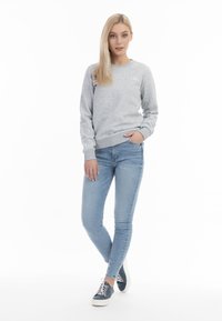 Grijze sweatshirt met geribbelde manchetten en zoom, gecombineerd met lichtblauwe skinny jeans en donkerblauwe sneakers, met witte veters en zool.