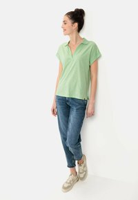 Groene polo-shirt met korte mouwen en een v-hals, gecombineerd met blauwe slim-fit jeans en beige sneakers, met lichte texturen en een ontspannen ontwerp.