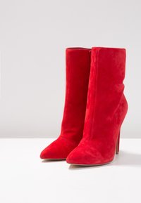 Stivali alla caviglia in suede rosso con punta affilata, alto tacco a stiletto e chiusura con cerniera liscia sul retro per una facile calzata.