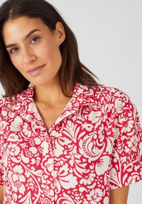 Camicia a maniche corte rossa con motivi grafici bianchi, colletto e dettagli con bottoni. Realizzata in tessuto leggero con una texture morbida.