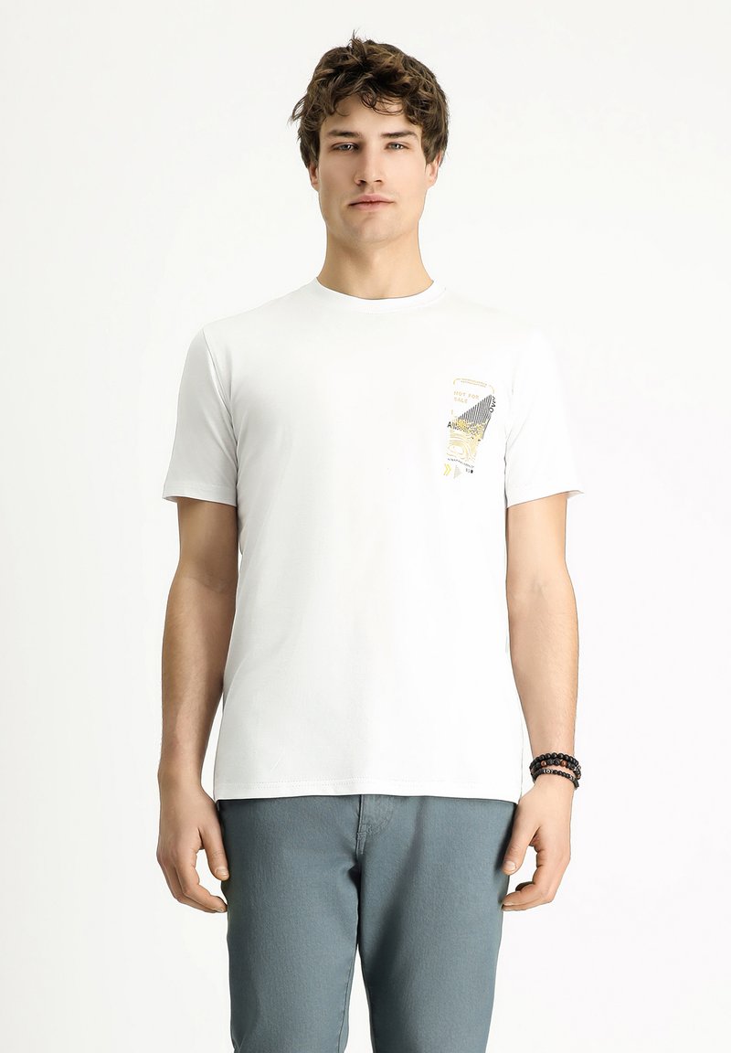 Camiseta de algodón blanca con un estampado en el bolsillo que presenta patrones abstractos en negro y amarillo. Mangas cortas y un diseño clásico de cuello redondo.