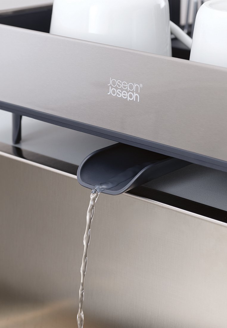 Abtropfgestell aus Edelstahl mit einem grauen Plastikauslauf. Das Wasser fließt aus dem Auslauf in ein Becken. Weiße Tassen sind darüber angeordnet.