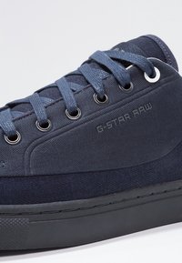 Mörkblå G-Star Raw sneaker med ovandel i tyg, metallhål, och platta skosnören, som visar sidologga och texturerad gummisula.