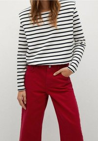 Blusa de manga larga a rayas en blanco y marino, combinada con pantalones rojos de pierna ancha y cintura alta. Presenta un ajuste relajado y un bolsillo frontal.