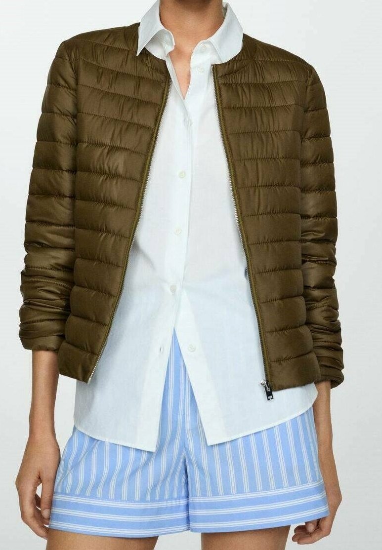 Giubbotto trapuntato verde oliva con scollatura rotonda, zip frontale e polsini a coste, abbinato a una camicia bianca con bottoni e pantaloni corti a righe blu.