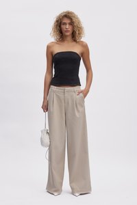Top nero senza spalline, pantaloni larghi color crema, borsa texture con dettagli di perline, modella in piedi con una mano in tasca.