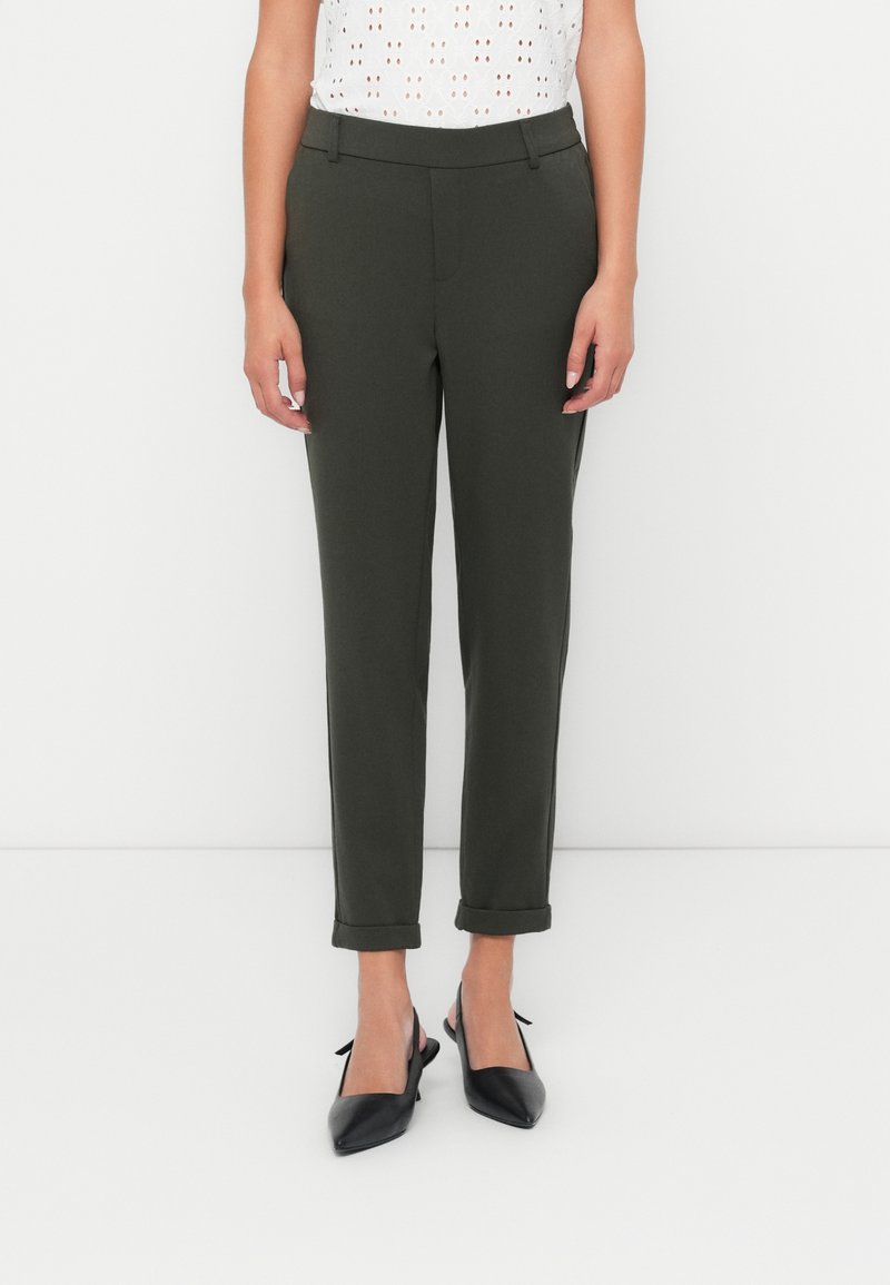 Olijfgroene tapered broek met een gladde textuur, voorzien van een gladde tailleband en opgerolde cuffs, gecombineerd met zwarte spitse schoenen.