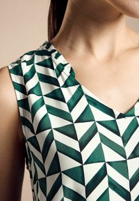 Top senza maniche verde e bianco con un motivo geometrico di triangoli alternati. Il tessuto appare liscio con una leggera lucentezza.