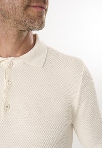 Gebreide poloshirt in off-white met een gestructureerd patroon, voorzien van een vlakke kraag en drie knopen aan de voorkant.