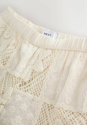 Biela sukňa s prepracovanými detailmi z čipky a výšivkou kvetín, pružný pás, označenie NEXT umiestnené v hornej časti.