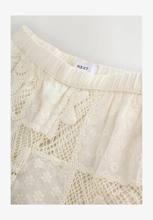Biela sukňa s prepracovanými detailmi z čipky a výšivkou kvetín, pružný pás, označenie NEXT umiestnené v hornej časti.