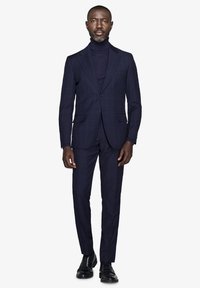 Marineblå stribede habit med en tætsiddende blazer og bukser med flad front, kombineret med en matchende turtleneck. Sorte lædersko fuldender looket.