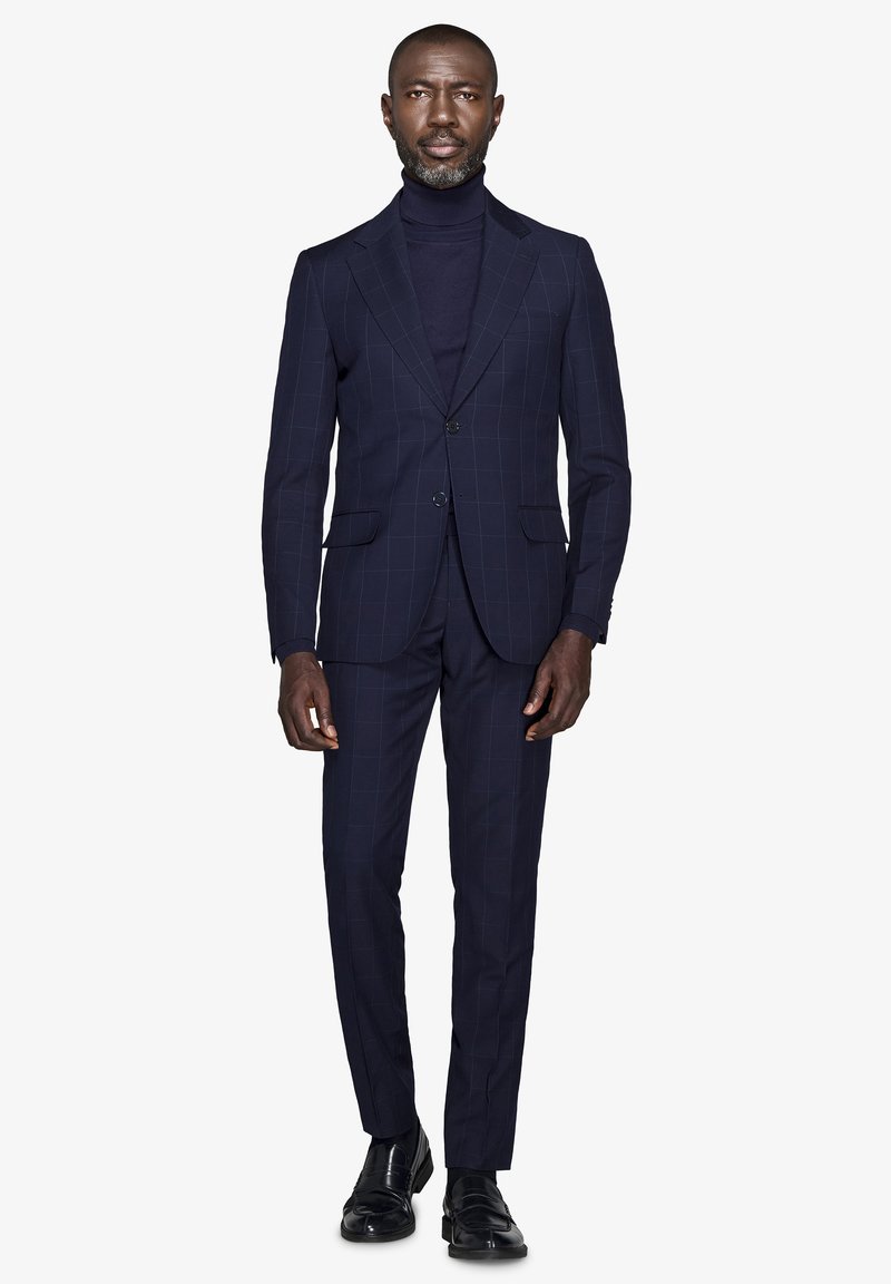 Marineblå stribede habit med en tætsiddende blazer og bukser med flad front, kombineret med en matchende turtleneck. Sorte lædersko fuldender looket.