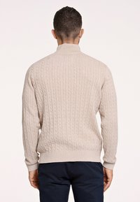 Maglione beige a coste con un colletto alto e polsini a coste. Il tessuto appare morbido, texturizzato e presenta motivi a cavo verticali.