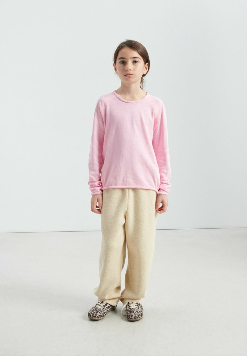 Chemise rose clair à manches longues avec ourlet brut, pantalon de survêtement beige et chaussures à enfiler à imprimé léopard. Design simple, textures douces, coupe décontractée.