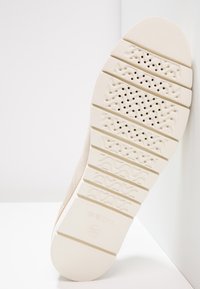 Semelle en caoutchouc blanc avec des motifs de grip texturés, perforations pour la respirabilité et détail de marque subtil. Finition lisse qui améliore la durabilité.