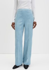 Pantalons en velours côtelé bleu clair à large jambe avec une taille haute et une texture à côtes verticales. Associés à des chaussures noires à bout pointu.