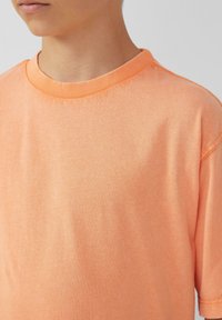 Korte mouwen, ronde hals t-shirt van lichtoranje katoen. Bevat een ribbelbare halslijn en een gladde textuur met subtiele stikseldetails.