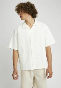 Chemise blanche à manches courtes en tissu texturé, col à encoches et bouton sur le devant. Caractéristiques : coupe décontractée et détails de motif subtils.