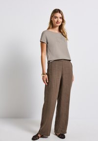 Top gris claro de manga corta con texto bordado, combinado con pantalones sueltos de lino marrón. Zapatos planos negros y una pulsera de oro completan el look.