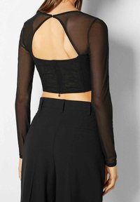 Top corto nero con lunghe maniche trasparenti, caratterizzato da un'apertura sul retro e bottoni, realizzato in materiale leggero. Finitura in tessuto testurizzato.