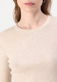 Beige strips ribbestrikket topp med rund hals, med en myk tekstur og tettsittende silhuett, som viser subtile vertikale linjer gjennom hele.