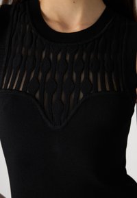 Top senza maniche nero con pannello trasparente caratterizzato da righe verticali testurizzate e dettagli in maglia sovrapposti nella scollatura e nel corpino.