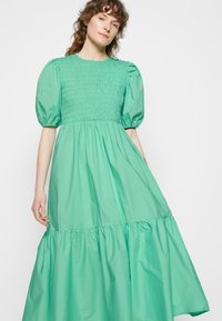 Vestido verde menta feito de tecido leve. Apresenta um corpete franzido, mangas curtas bufantes e uma saia em camadas. Textura suave.