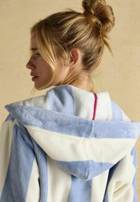 Riba mustriga kapuutsiga vannituba helesinises ja valges fliisis, millel on pehme tekstuur, suur kapuuts ja punane aktsent sisekaeluses.